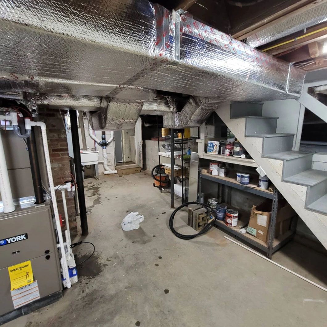 A basement with a furnace , stairs , shelves and a bike.