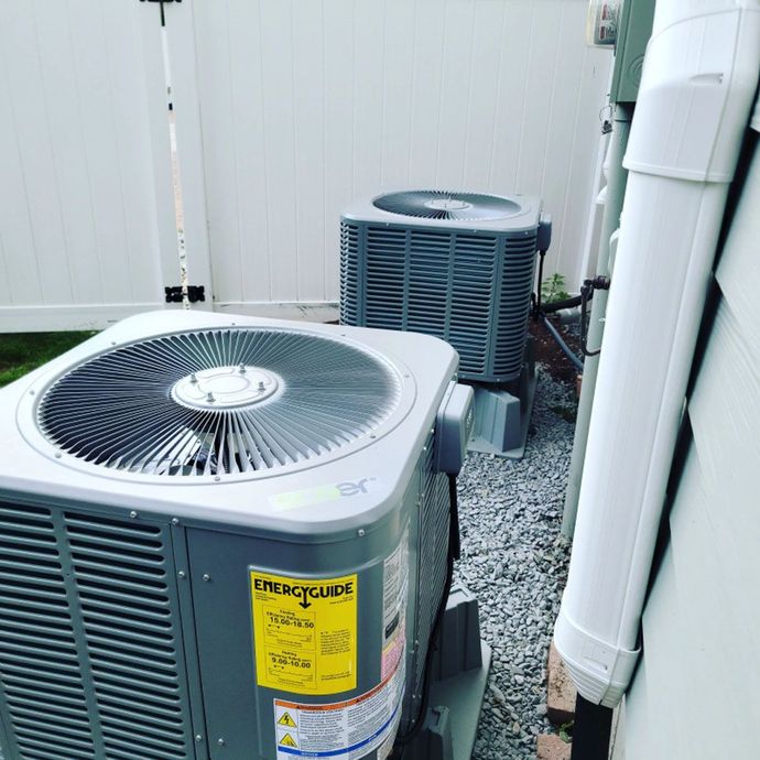 Two air conditioners are sitting next to each other on the side of a house.