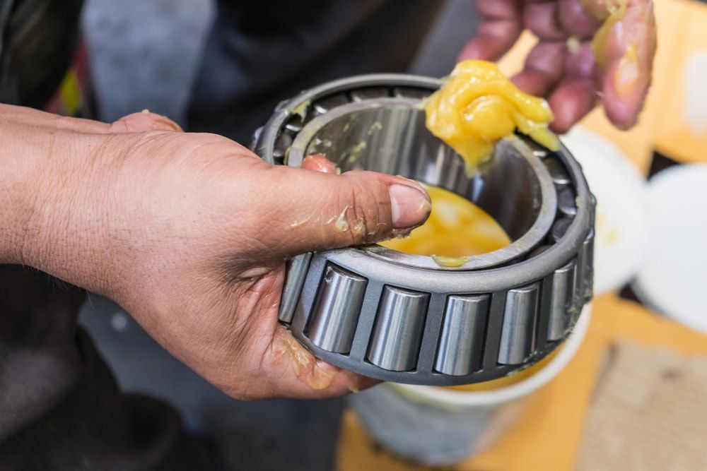 Hands Applying Yellow Industrial Grease to the Rollers — JNL Crankshaft Services in Palmerston City, NT