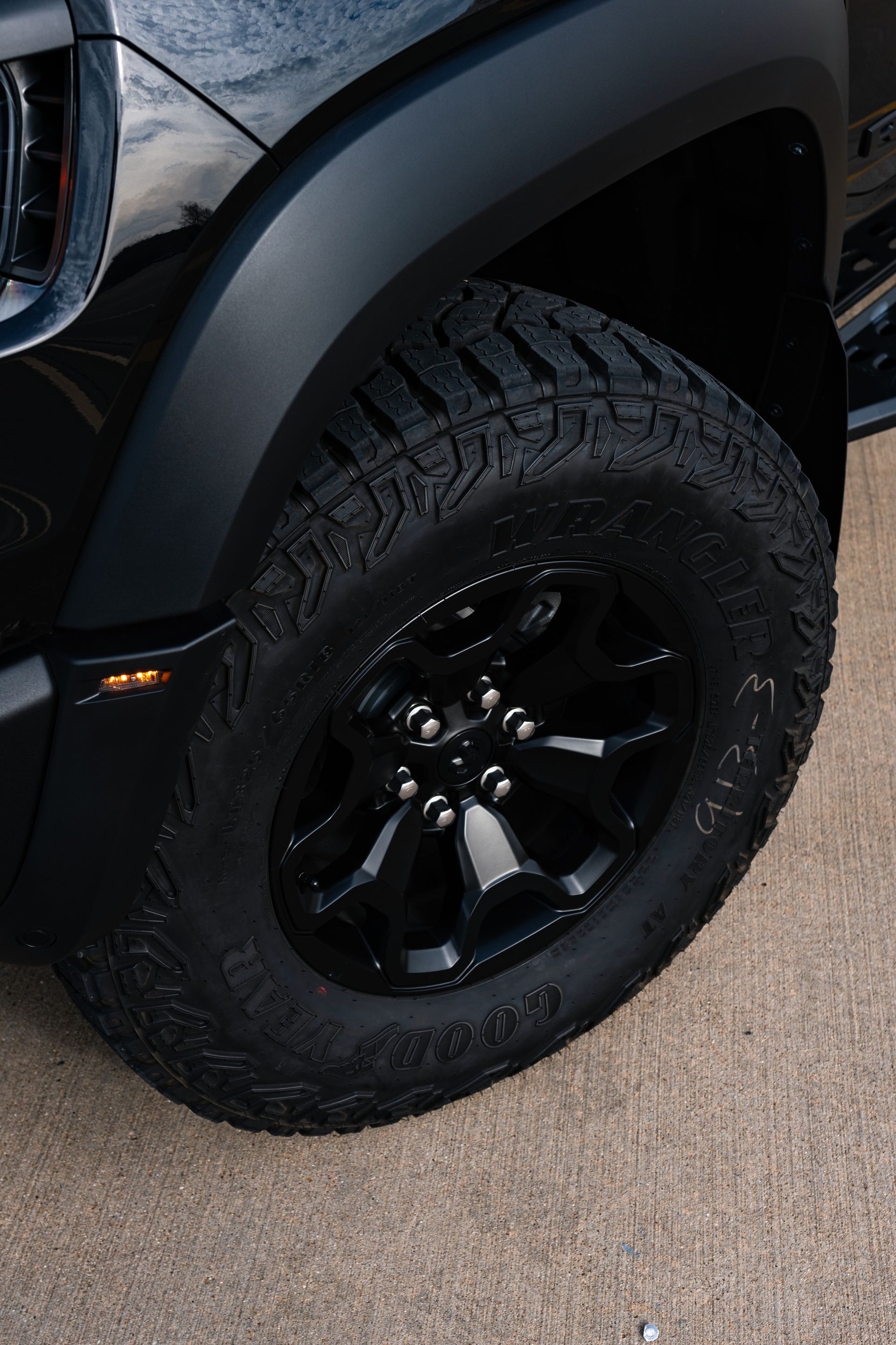 A close up of a black truck 's tire and wheel.