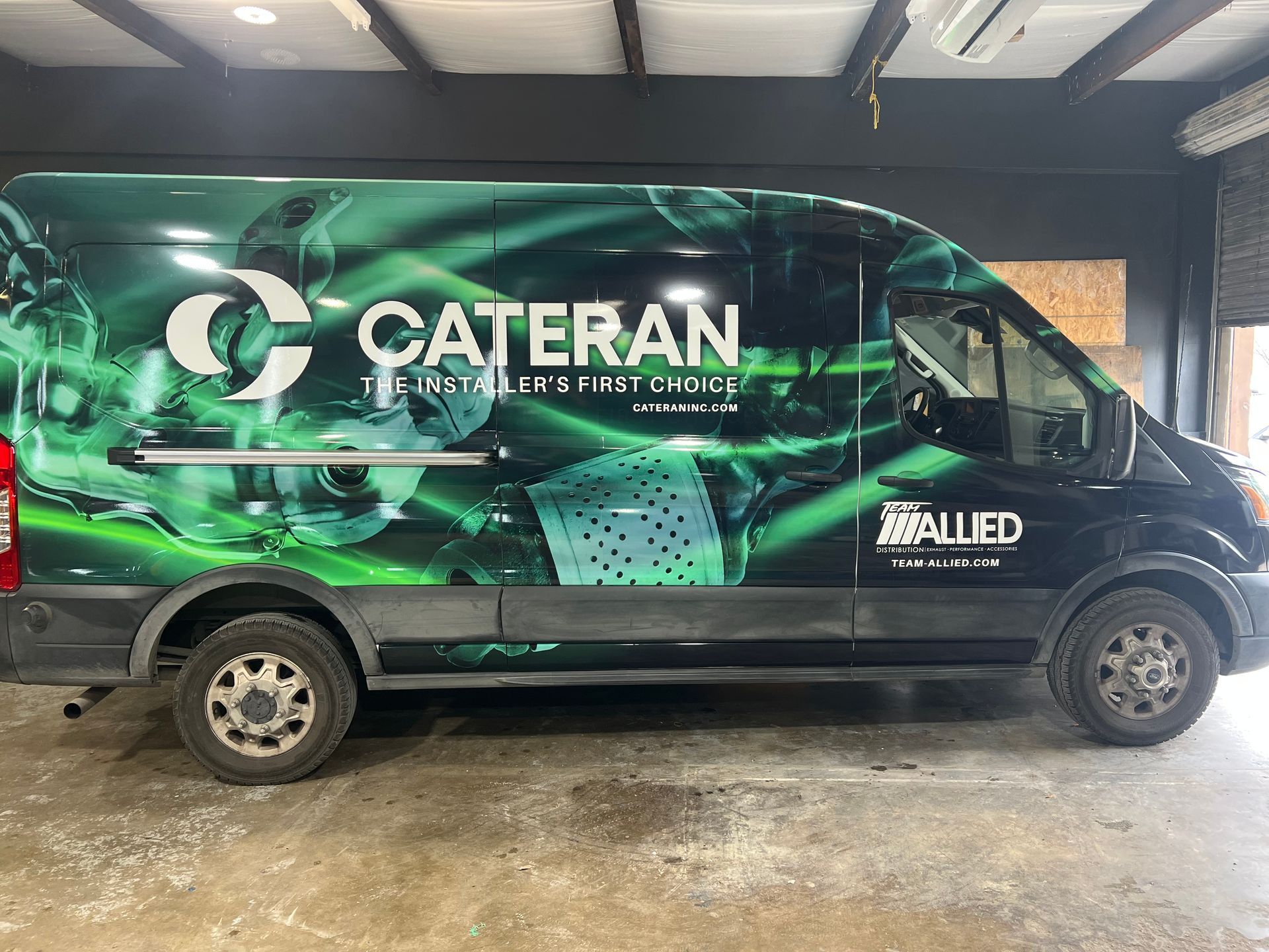 A black Cateran catering van with a green and blue design parked on a concrete floor.