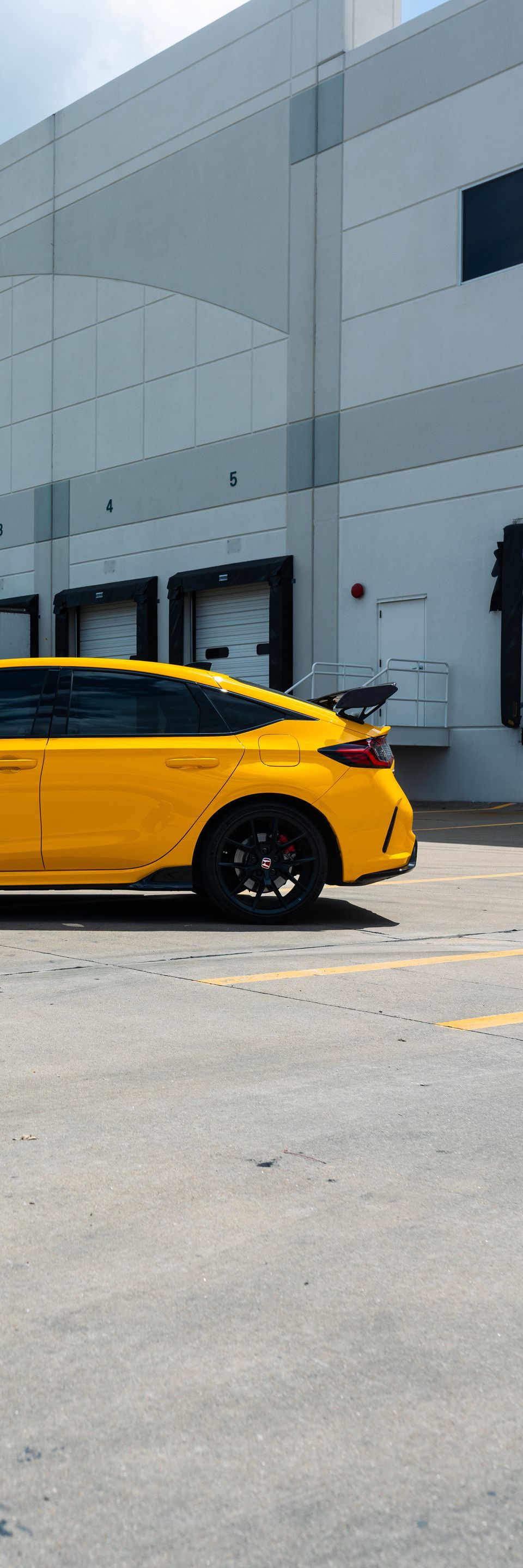 A bright yellow car is parked in front of a large grey warehouse building.