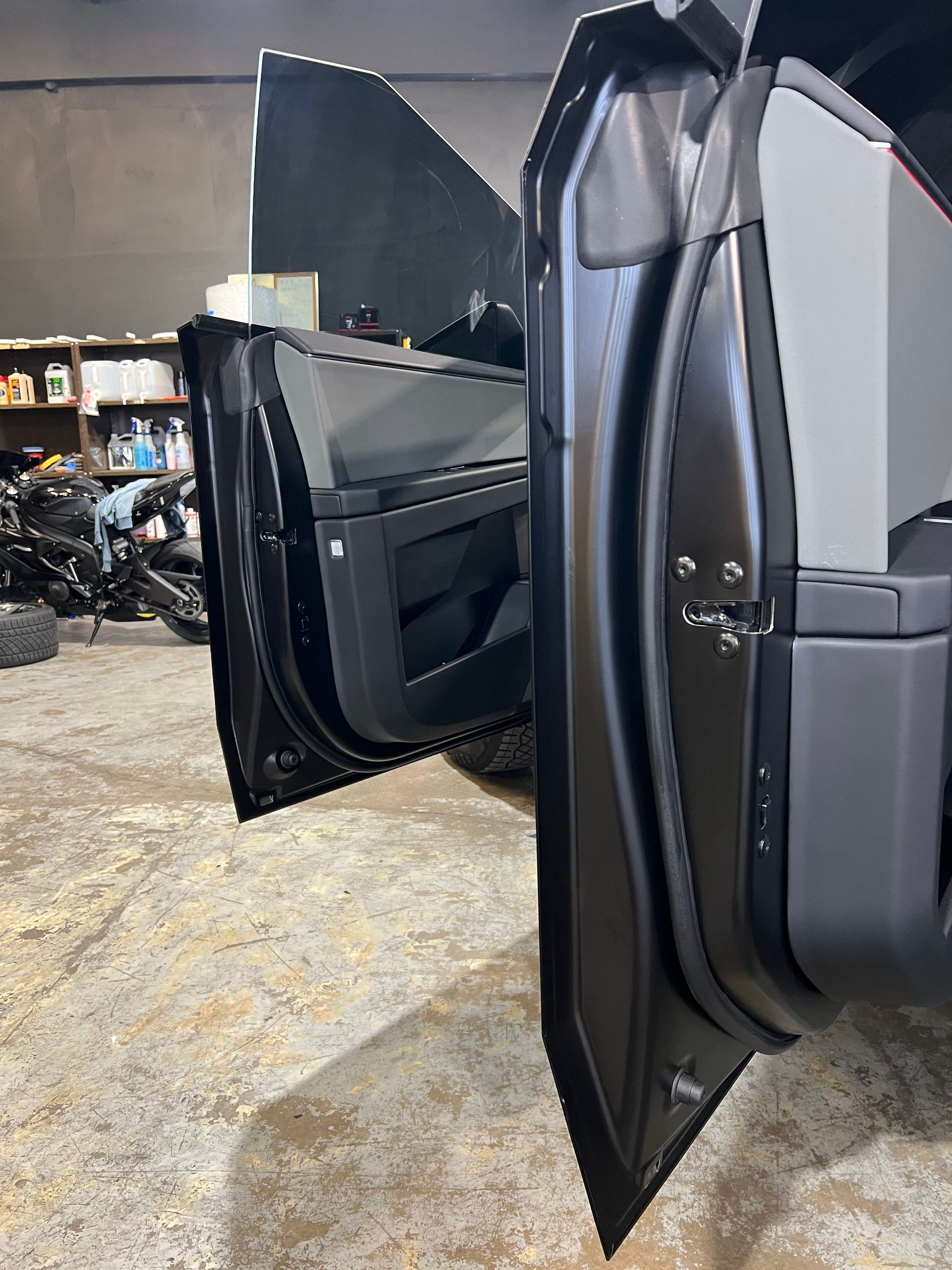 Open black car doors, revealing interior and a cluttered shop background.