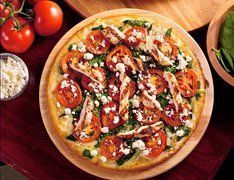 Tomato and cheese pizza on a wooden board, garnished with fresh spinach, feta cheese, and cooked tomatoes.