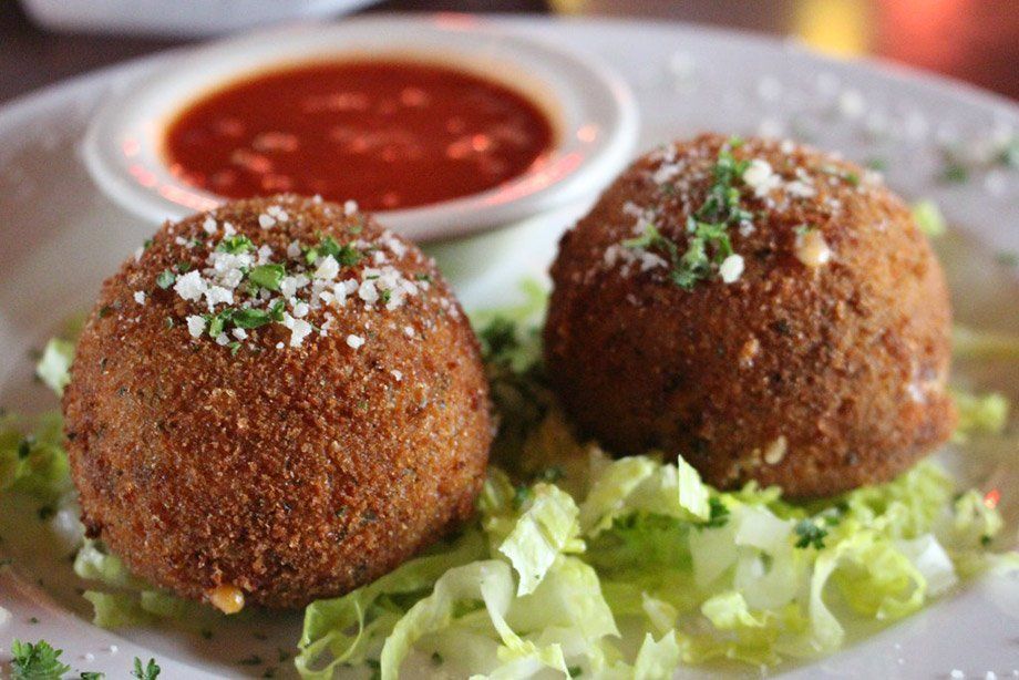 Two fried arancini balls on a bed of lettuce, served with marinara sauce.