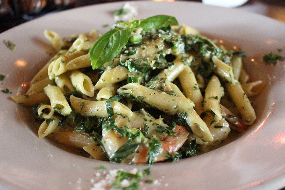 Penne pasta in creamy green sauce with basil garnish, served in a white bowl.