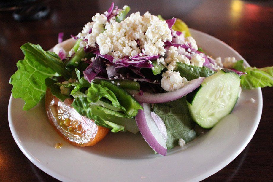 Greek salad with crumbled feta, red onion, cucumber, tomato, and lettuce on a white plate.