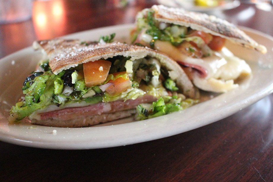 Two halves of a sandwich on a plate, filled with meat, cheese, lettuce, and tomato.