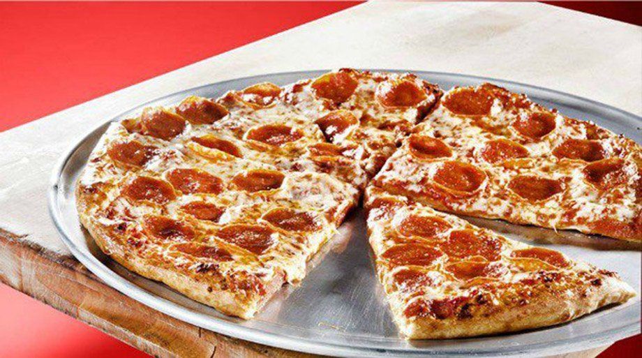 Pepperoni pizza on a metal tray, sliced into sections, with a red background.