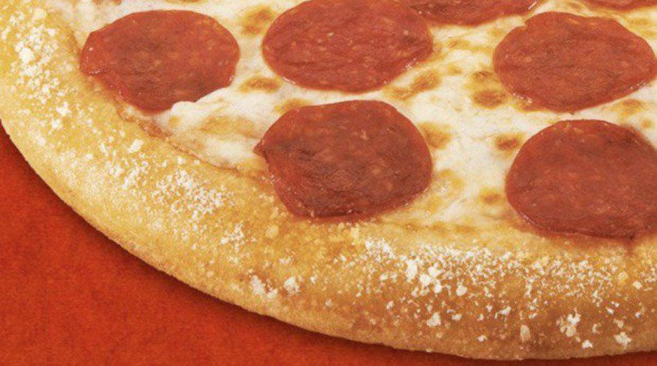 Close-up of a pepperoni pizza on a red surface. The crust is golden brown, and the cheese is melted.