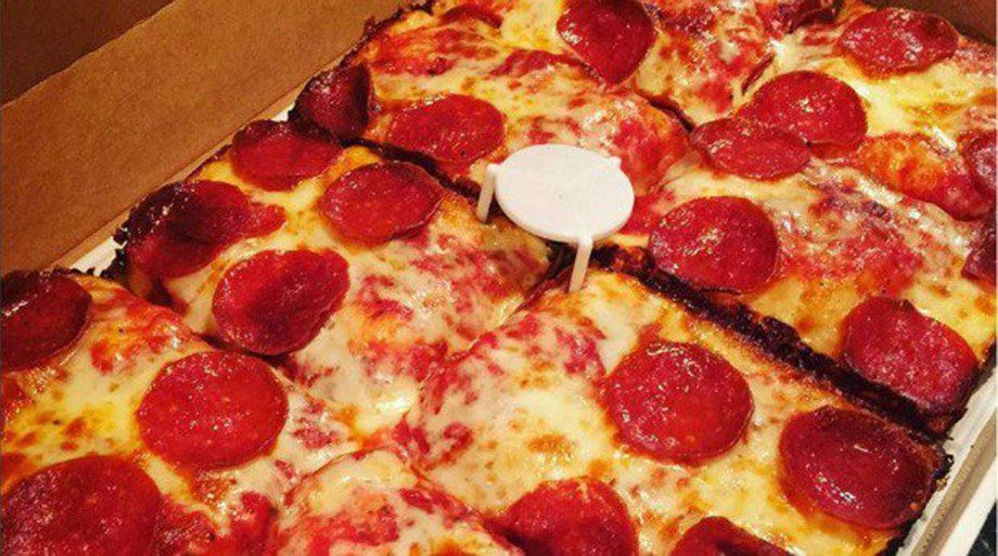 Square pepperoni pizza in a box, cut into squares with melted cheese and a white plastic support in the middle.