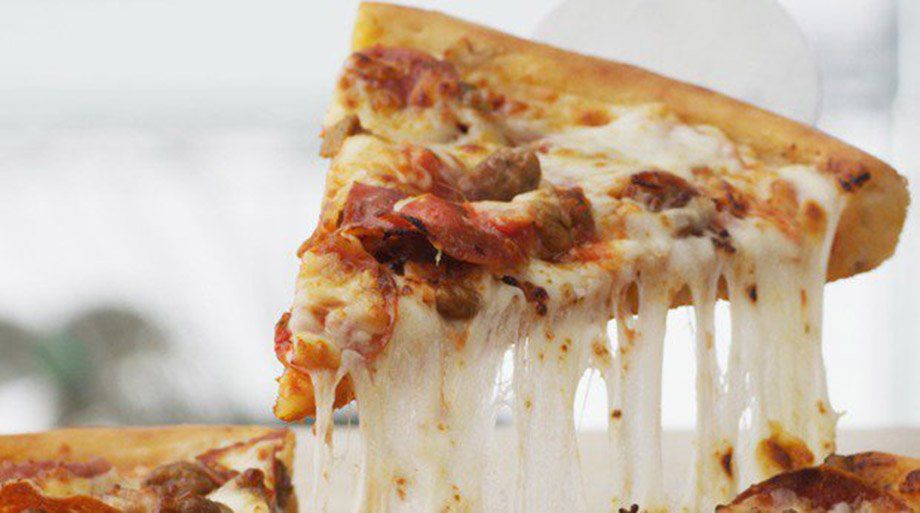 Slice of pizza being lifted, with melted cheese stretching downward. Toppings include pepperoni and sausage.