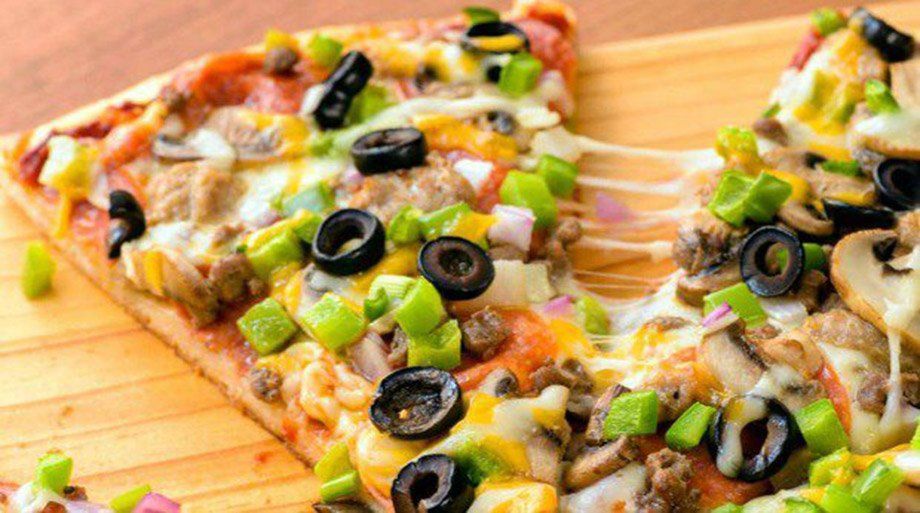 Pizza slice with melted cheese, vegetables, and olives on a wooden board. One slice being pulled away, cheese stretching.