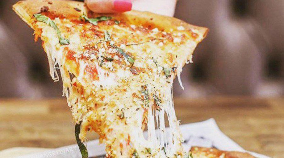 Hand holding a slice of pizza with stretching melted cheese, basil, and sauce.