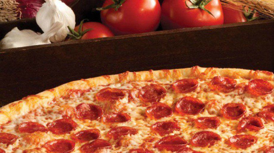 Pepperoni pizza with fresh tomatoes, garlic, and onions in the background.