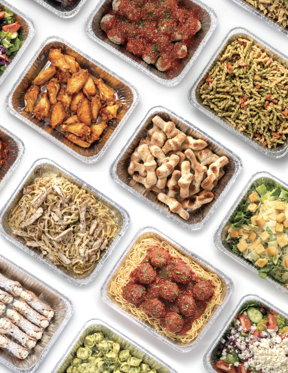 Assorted prepared food dishes in foil containers, including pasta, chicken, meatballs, and salads.