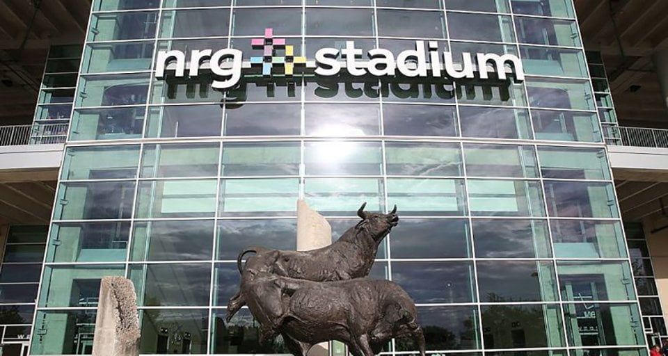 NRG Stadium entrance with a bull statue in front. The building has a glass facade and the stadium name in large white letters.