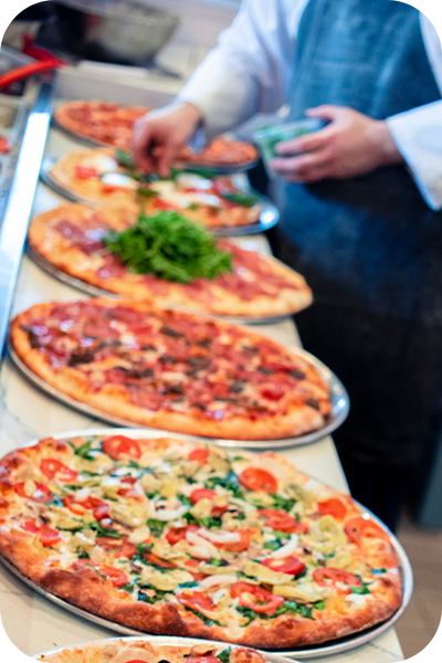 Chef adding toppings to several pizzas lined up on a counter.