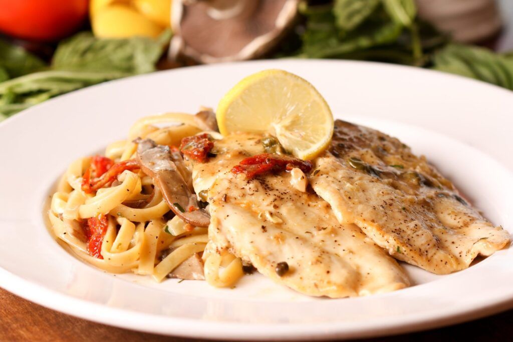 Pasta with fish fillets on a white plate, garnished with lemon.