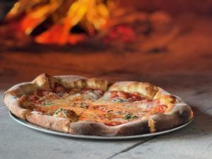 Pizza on a plate, in front of a wood-fired oven with visible flames.