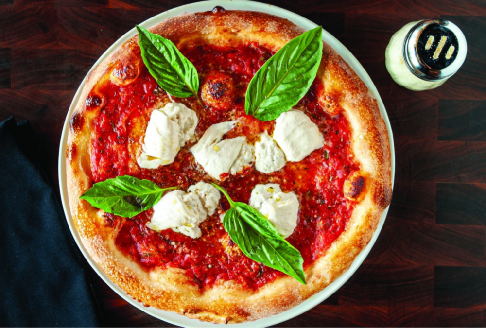 Pizza with tomato sauce, ricotta cheese, and basil on a white plate.