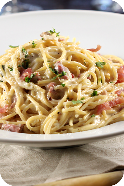 Spaghetti carbonara in a white bowl, topped with parsley. Bacon and creamy sauce are visible.