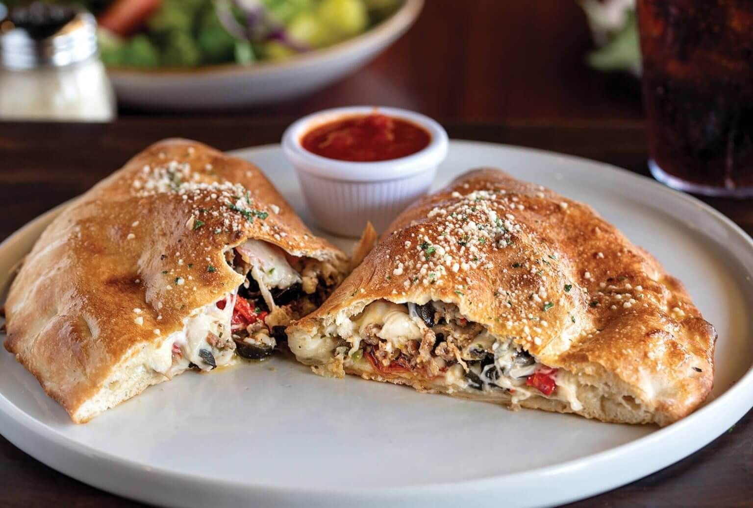 Calzone cut in half on a plate with dipping sauce, showcasing filling.