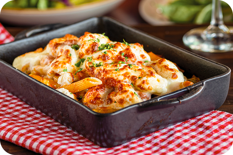 Baked pasta dish in a black rectangular pan, topped with melted cheese and parsley, on a red and white checkered napkin.