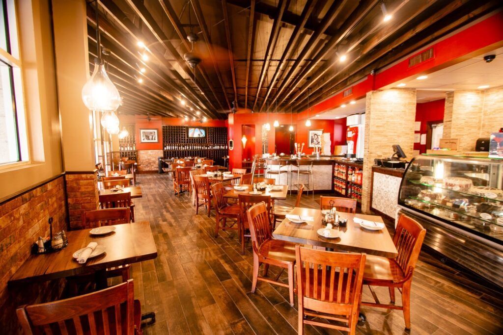 Restaurant interior with wooden tables, chairs, and floors. Red and brown walls, with bright overhead lighting.