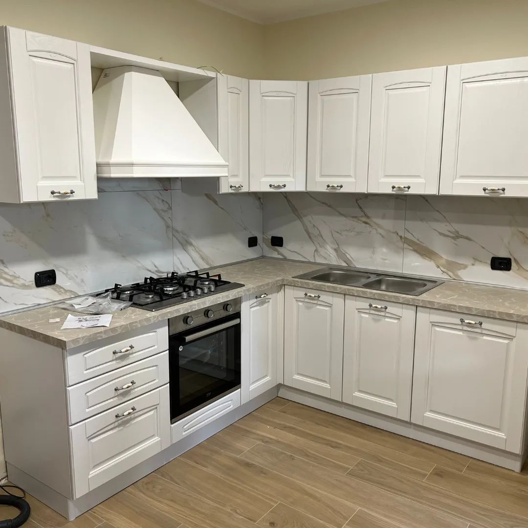 Una cucina con mobili bianchi, fornelli e lavello.