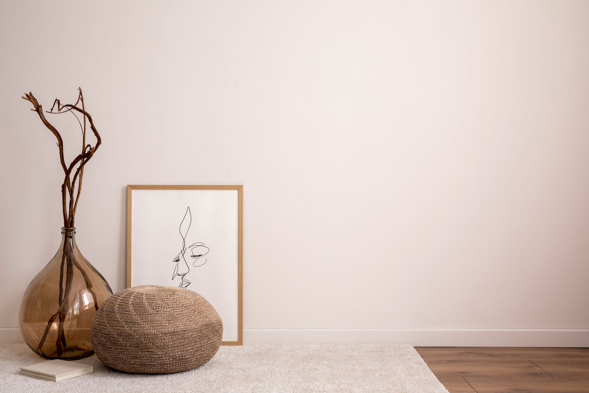 Un soggiorno con un vaso, un pouf, un dipinto e un quadro sul muro.