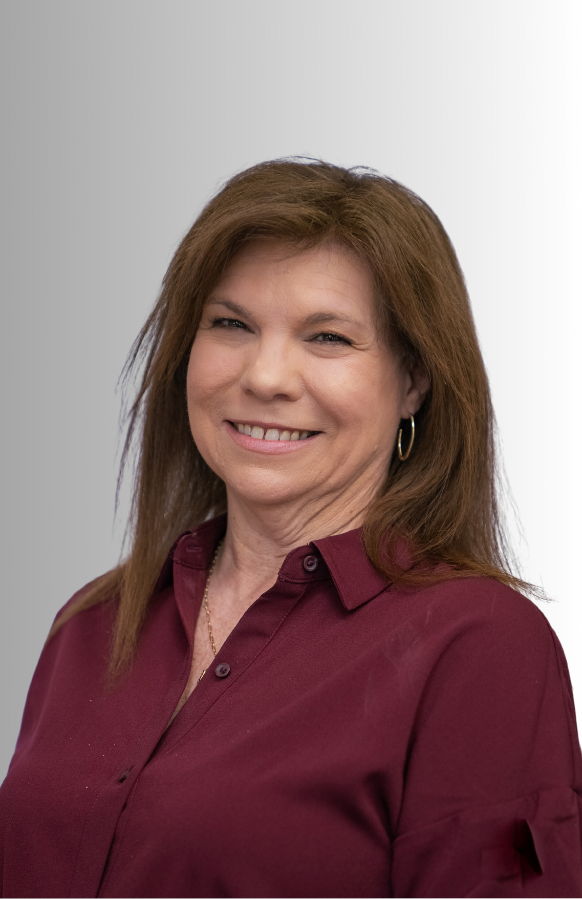 A woman wearing a red shirt and earrings is smiling for the camera.
