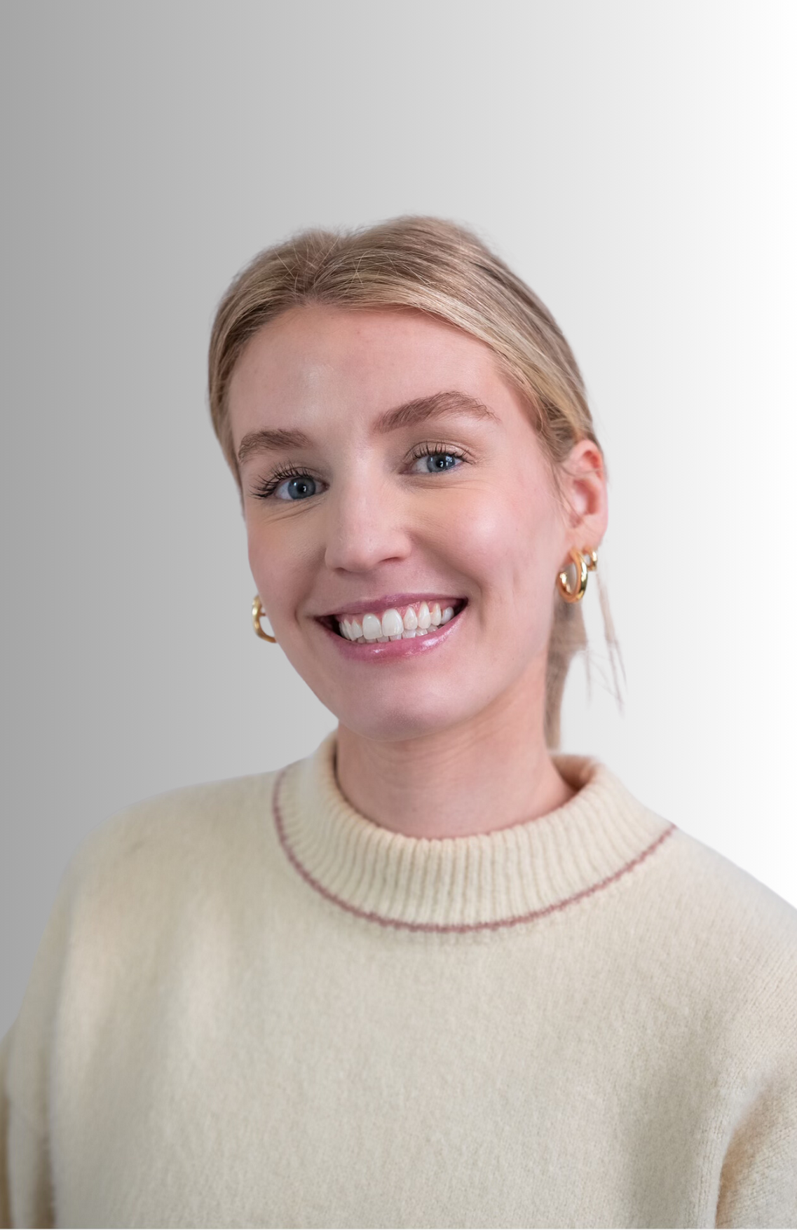 A woman wearing a white sweater and earrings is smiling for the camera.