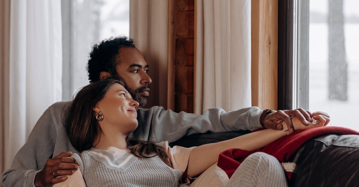 A man and a woman are sitting on a couch in front of a window.