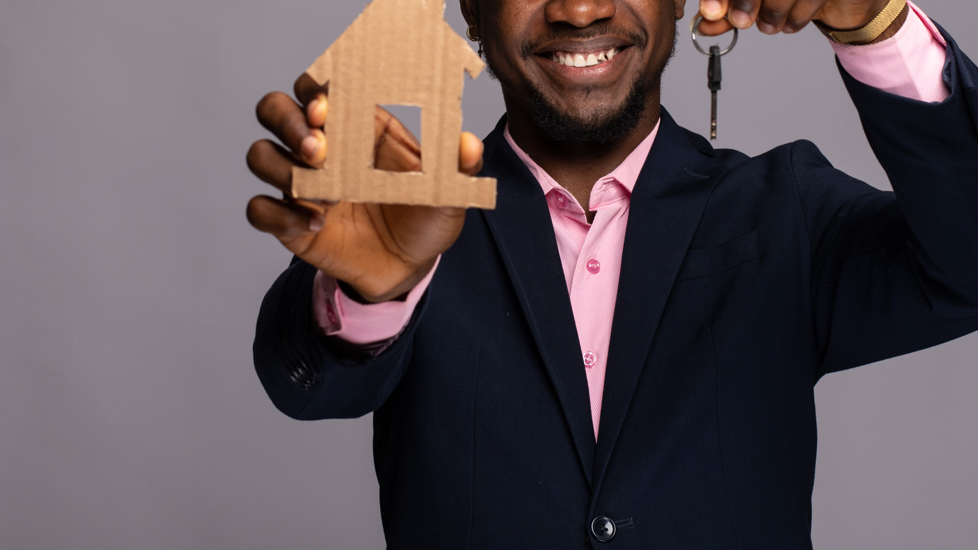 A woman is sitting at a desk holding a small house and keys.
