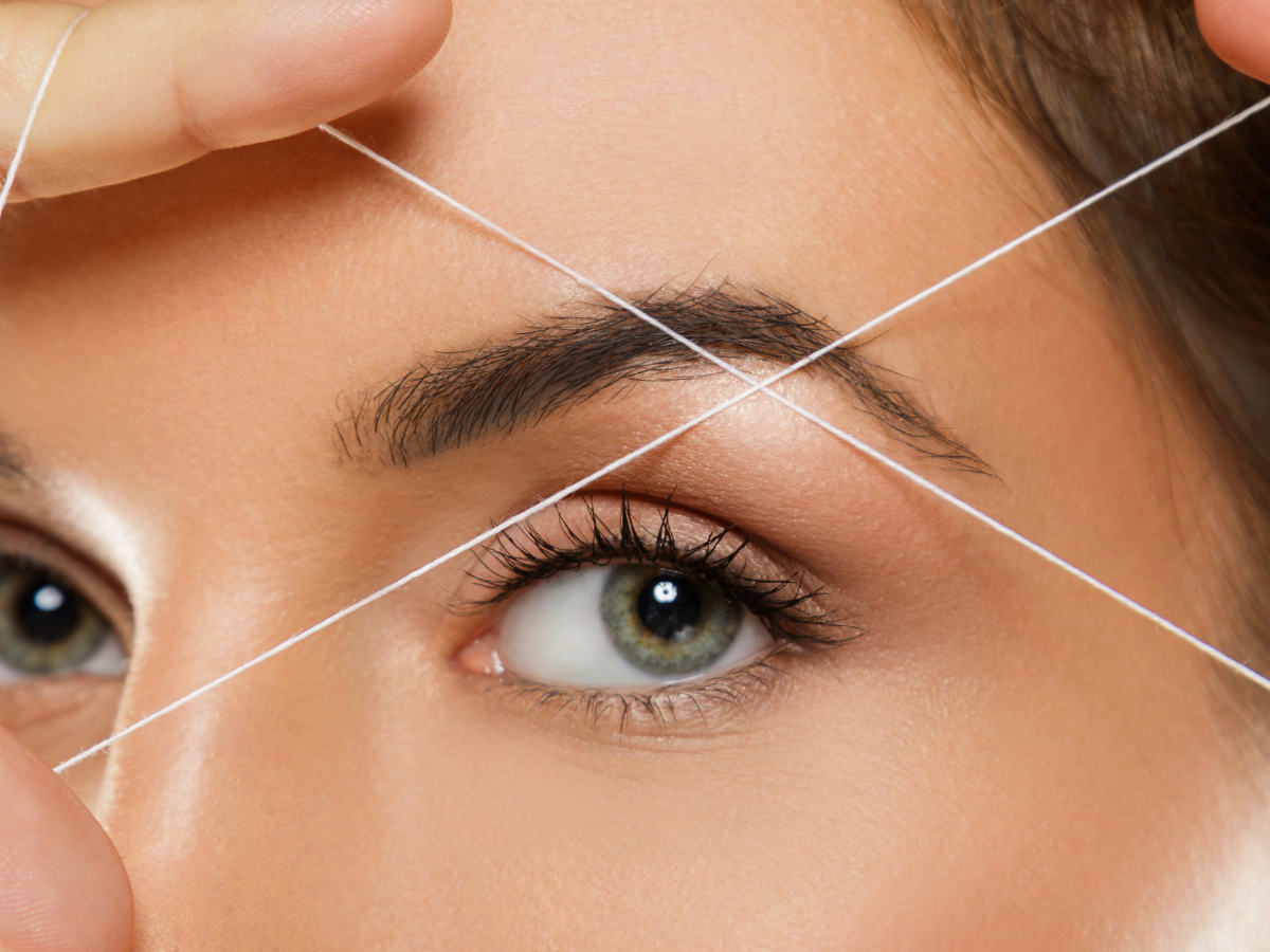Woman's eye and eyebrow with threading strings, ready for eyebrow shaping.