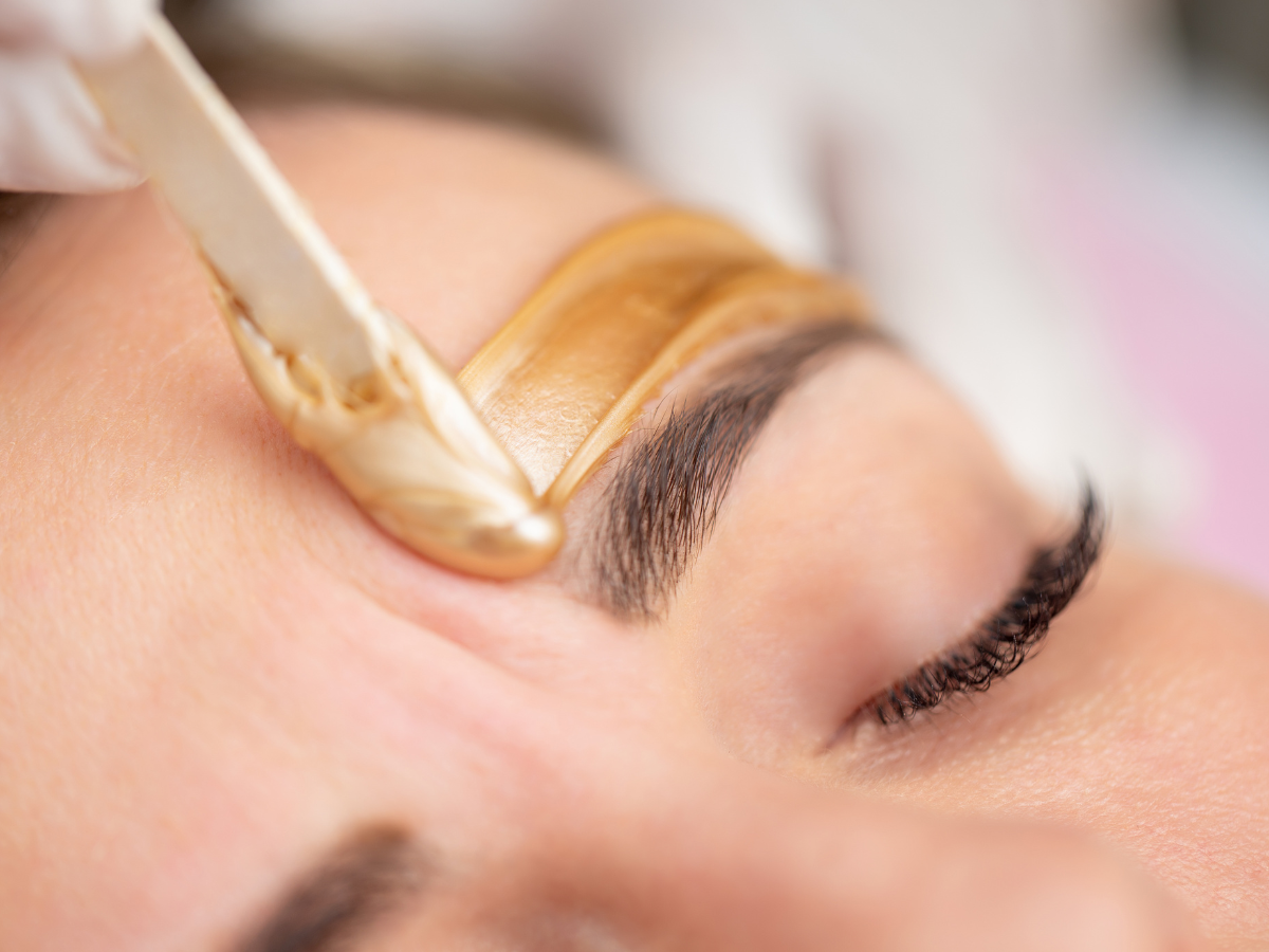 Wax being applied to an eyebrow with a spatula.