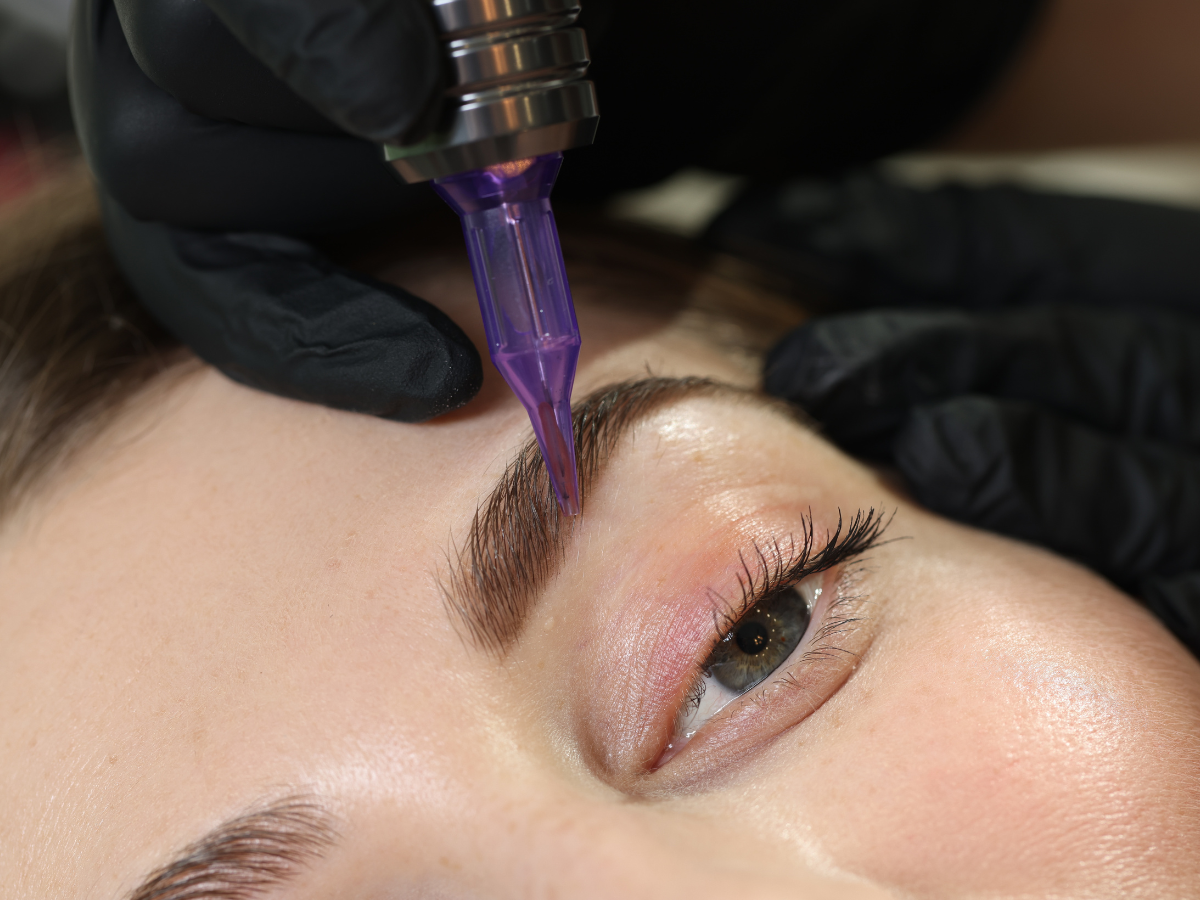 Eyebrow microblading in progress: gloved hand using a tattoo pen on a woman's brow, close-up shot.