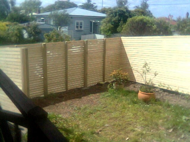 A wooden fence surrounds a lush green yard with a house in the background.