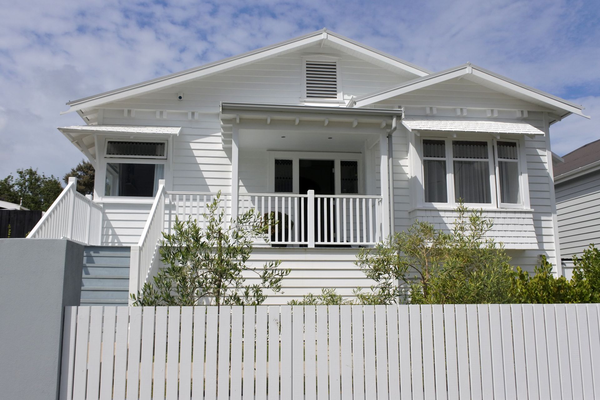 The front porch of a house with a wooden door and a white railing.
