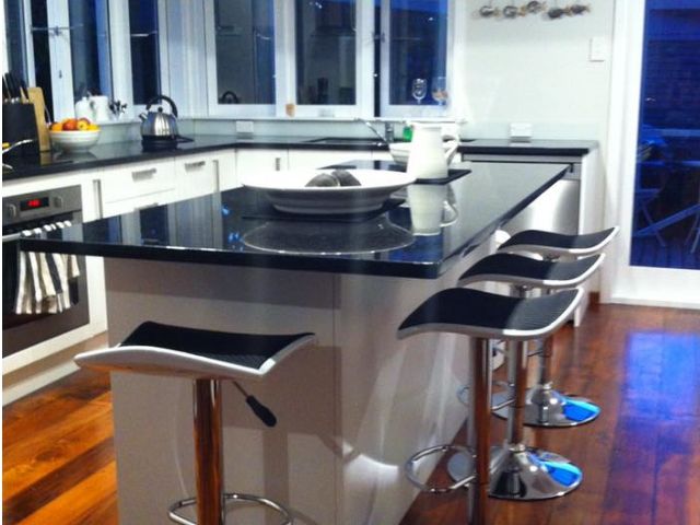 A kitchen with a black counter top and stools.