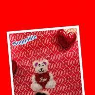 Huggable teddy bear ornament on a red patterned background with a shiny red heart