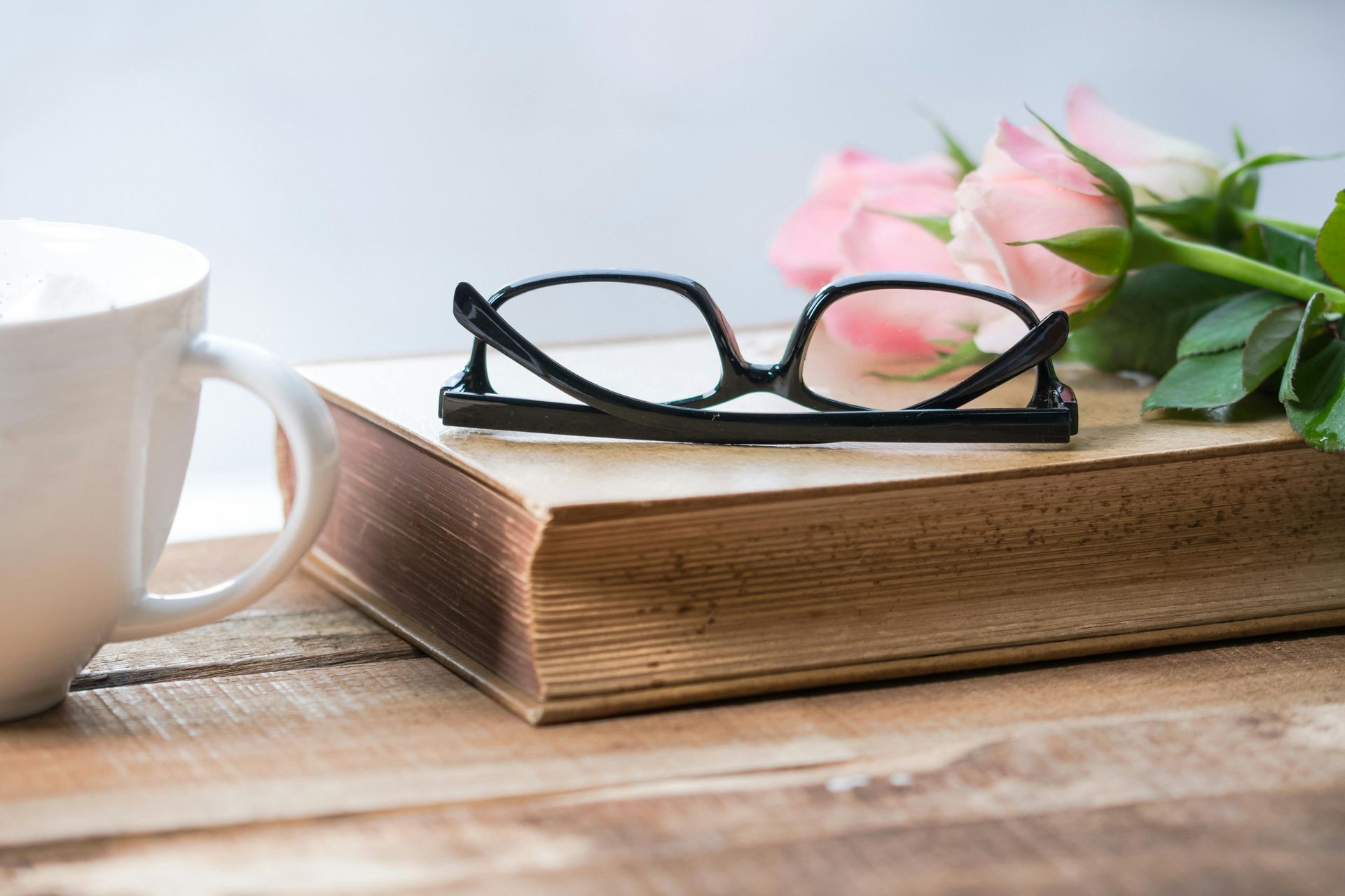 A pair of glasses is sitting on top of a book next to a cup of coffee.