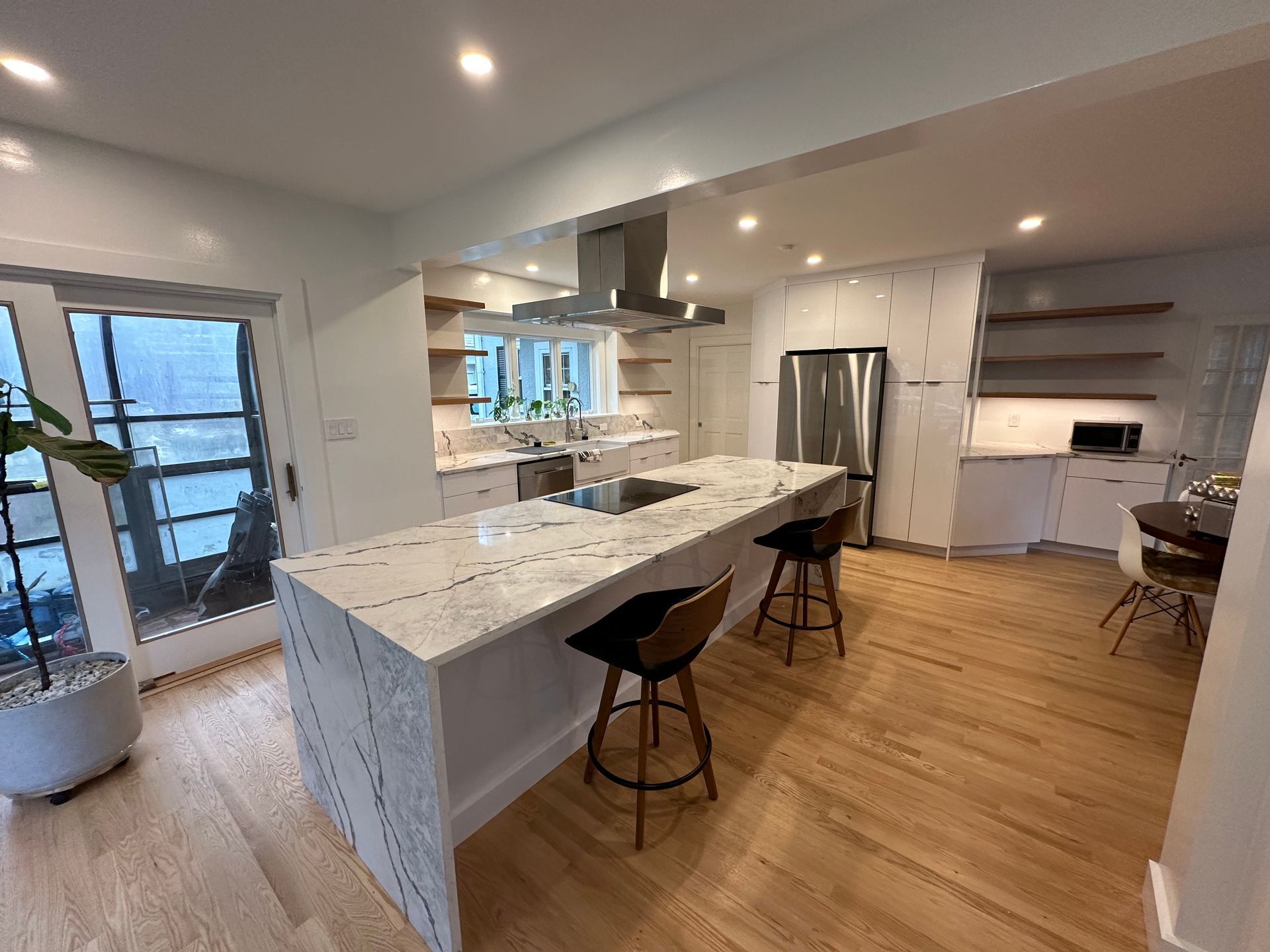 Modern kitchen with white cabinets, marble countertops, stainless steel appliances, and wood floors.
