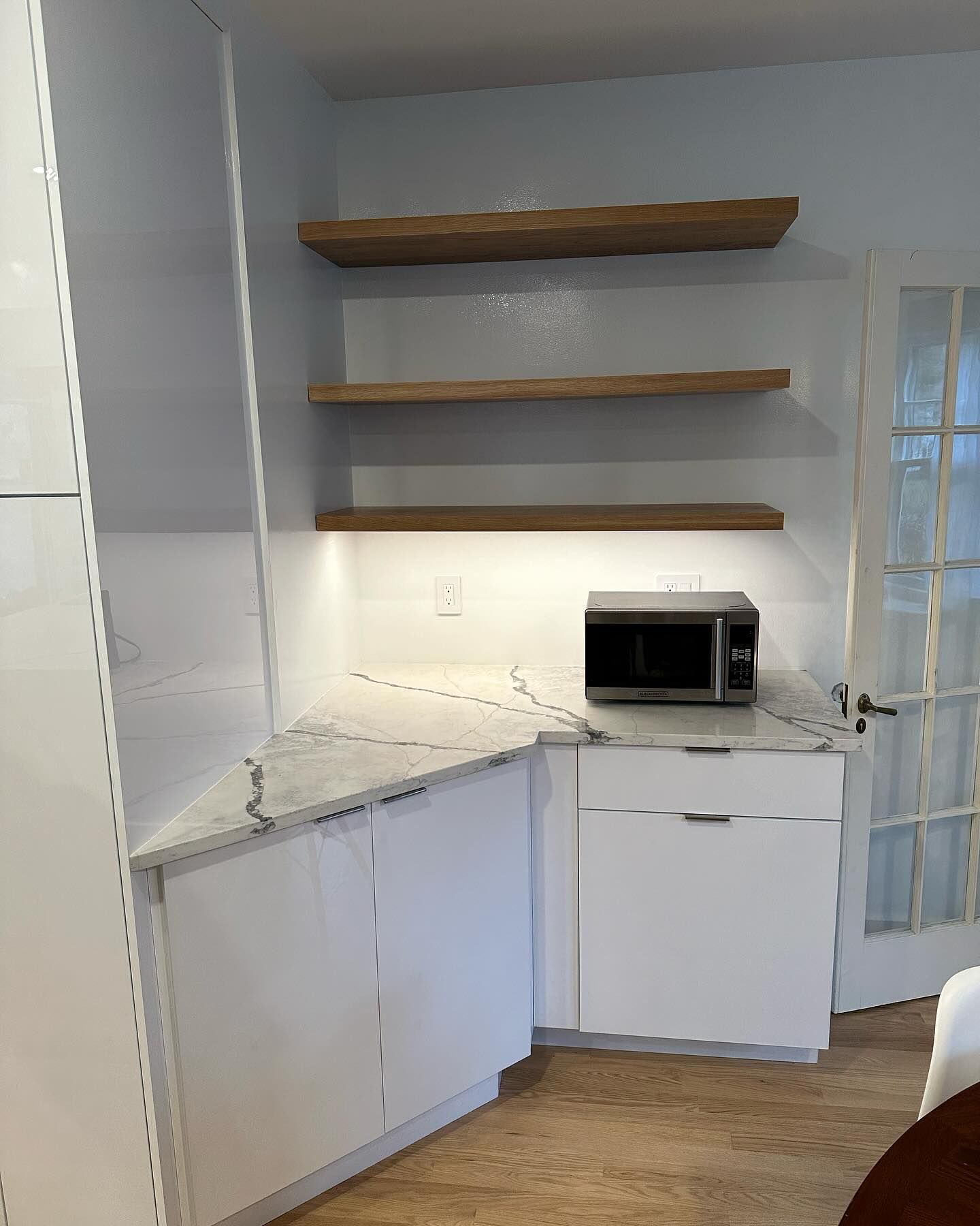 White kitchen corner with floating wood shelves, built-in cabinets, and a microwave.