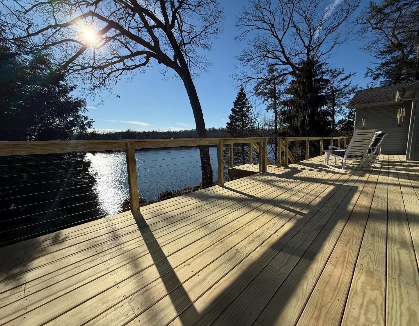 Wooden deck overlooking a lake, with trees and a sunny sky.