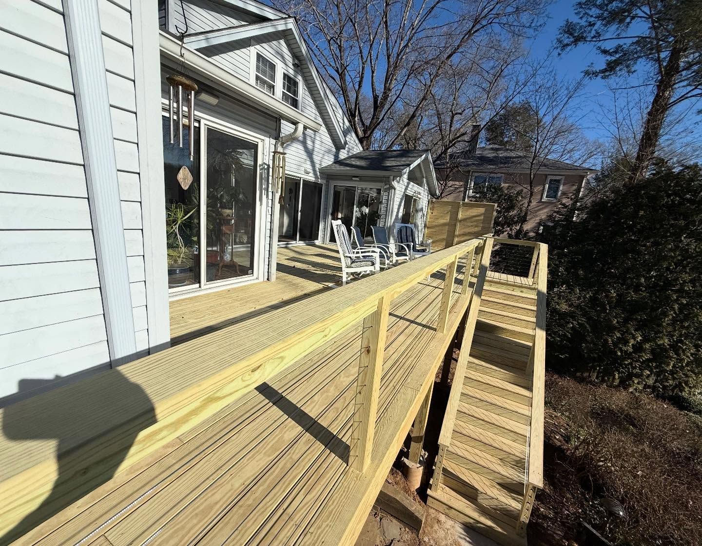 Wooden deck with railing and stairs extending from a light-colored house.