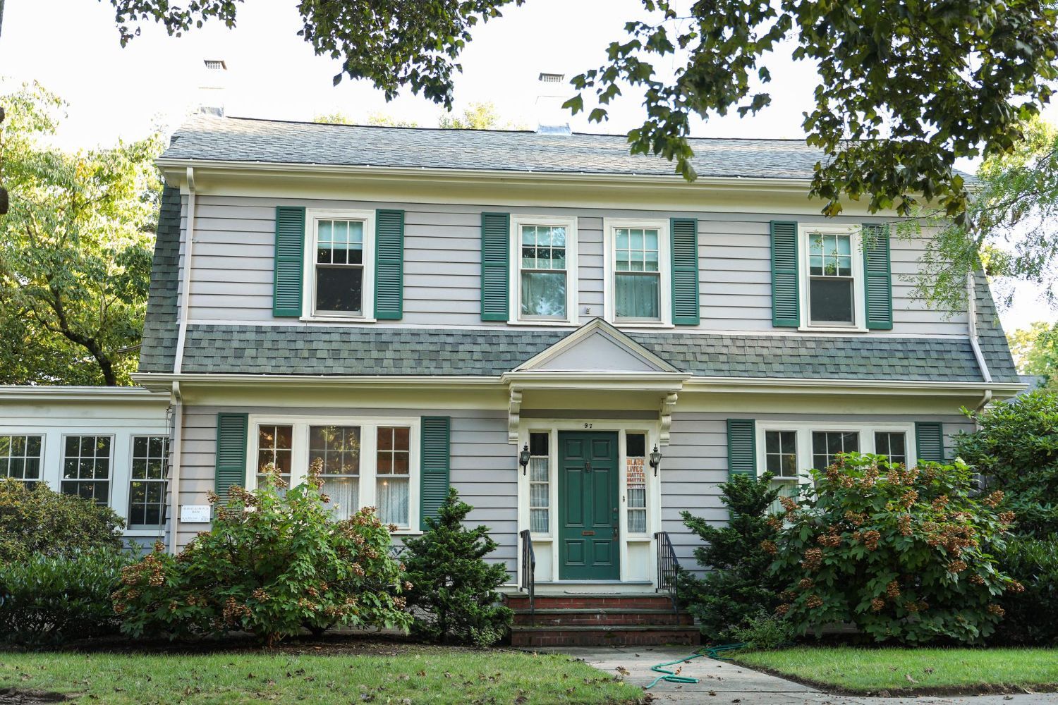 Two-story house with light grey siding, green shutters, and a green front door.