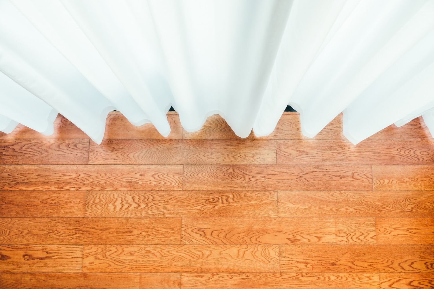 White curtains over a brown wooden floor, overhead shot.