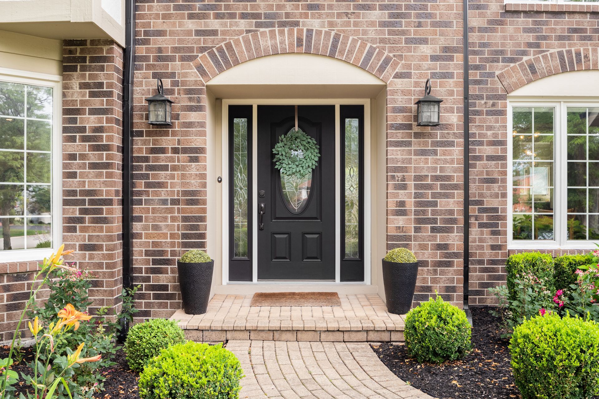 A brick house with a black front door and a brick walkway leading to it.